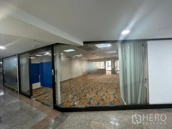 办公空间 出租 - 玻璃落地门面办公室，室内明亮、彩色地毯，从走廊可见。