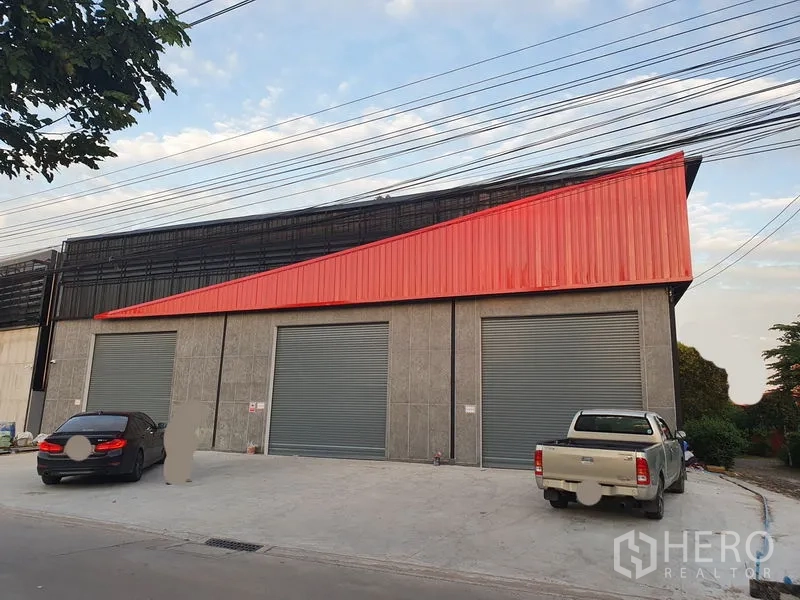 คลังสินค้า ให้เช่าในPak Kret, Nonthaburi - ด้านหน้าอาคารมีประตูม้วนสีเทาขนาดใหญ่ 3 ช่อง พร้อมพื้นที่จอดรถกว้าง