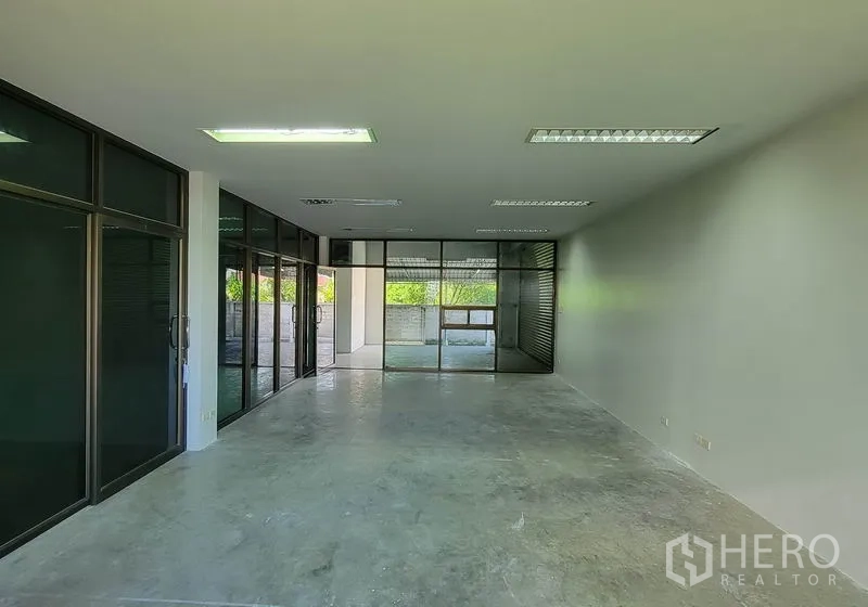 Warehouse for rent in Sam Phran, Nakhon Pathom - Spacious office area with floor-to-ceiling glass partitions and concrete floor.