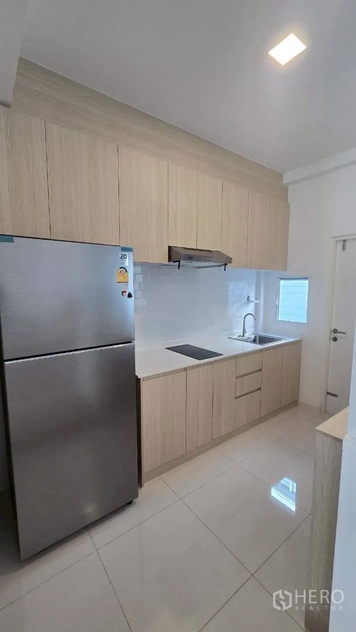 联排别墅 for rent in Prawet, Bangkok - 浅木色一字型厨房，柜体、灶台、烟机、水槽与不锈钢冰箱齐全。