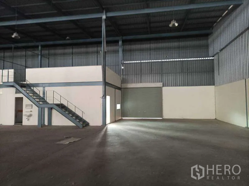 工厂 for rent in Ban Phaeo, Samut Sakhon - 仓库内部视角，夹层、楼梯与大型卷闸入口一应俱全。