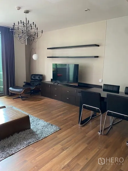 Condominium for rent in Khlong Toei, Bangkok - TV wall with floating shelves, long cabinet, lounge chair and dining table in a modern condo living space.
