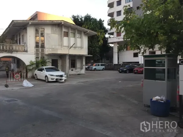 零售空间 出租在Khlong Toei, Bangkok - 两层建筑带拱门与岗亭，前方为大面积硬质停车场，位于Thonglor片区。