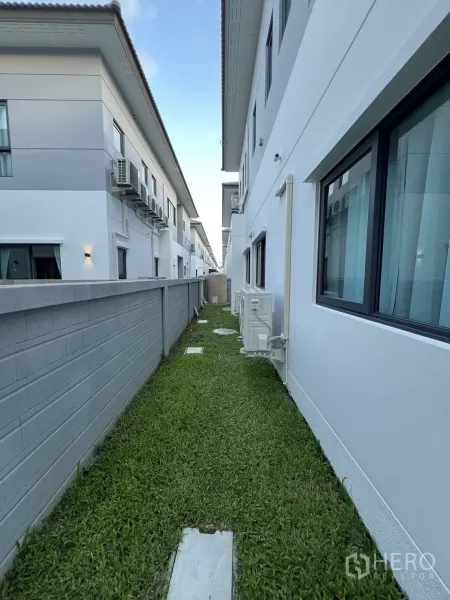 Detached House for rent or sale in Bang Phli, Samut Prakan - Narrow lawn between homes with privacy wall and exterior air-conditioning units.