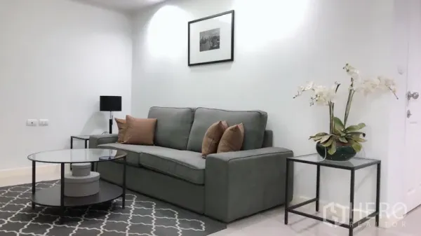 Condominium for rent or sale in Khlong Toei, Bangkok - Bright living room with gray sofa, glass coffee table, wall art, and orchid on a side table at Waterford Sukhumvit 50.