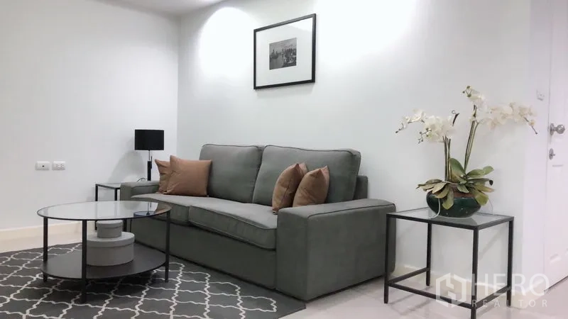 Condominium for rent or sale in Khlong Toei, Bangkok - Bright living room with gray sofa, glass coffee table, wall art, and orchid on a side table at Waterford Sukhumvit 50.