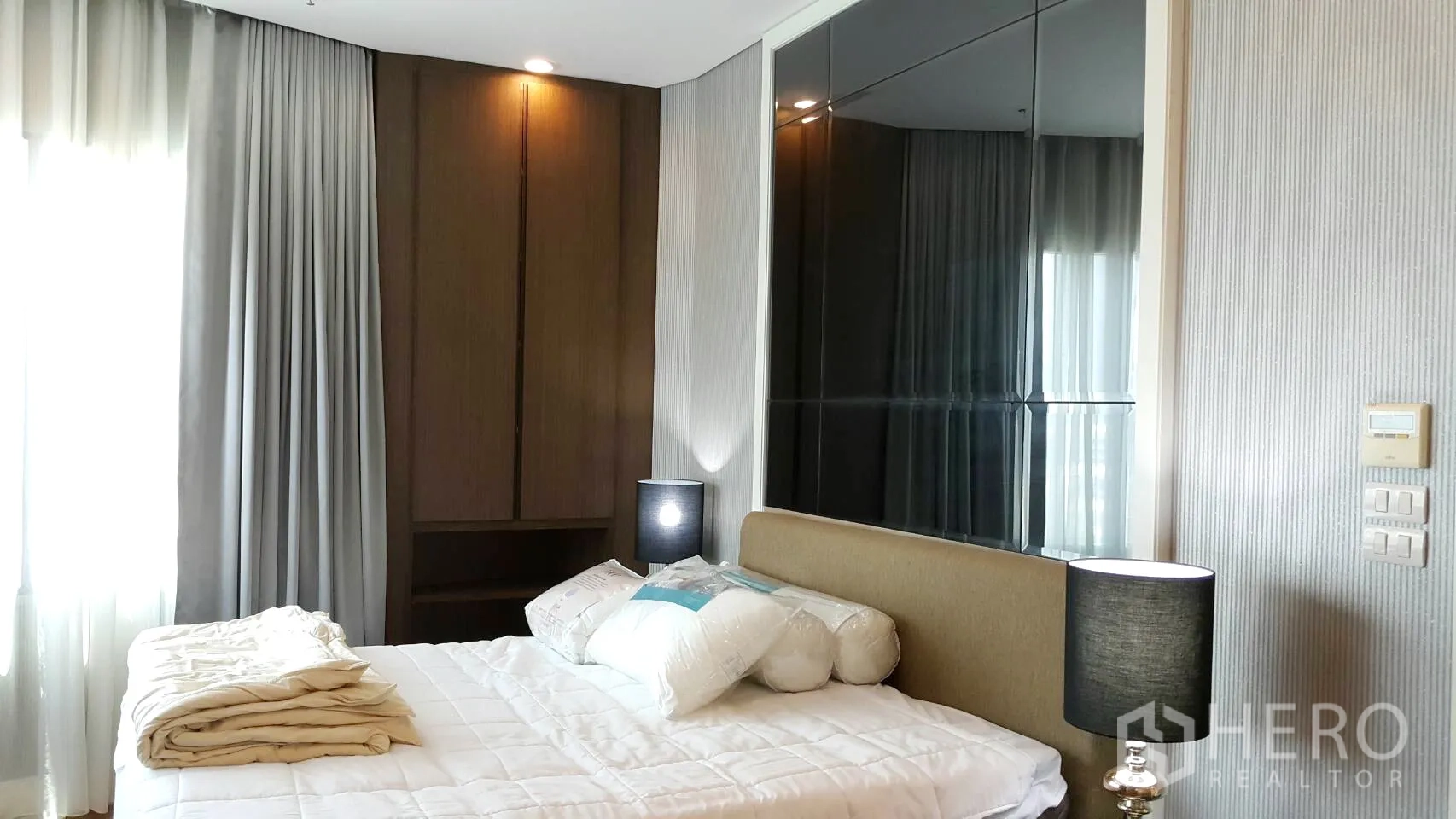 Condominium for rent in Khlong Toei, Bangkok - Bright bedroom with double bed, bedside lamps and mirrored accent wall.