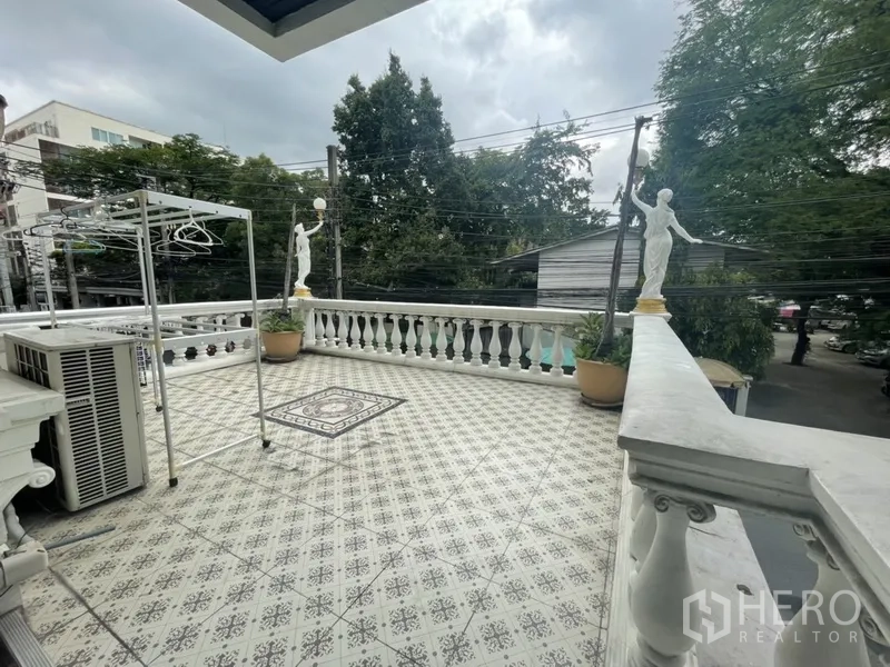 Home Office for rent or sale in Watthana, Bangkok - Expansive tiled terrace with classical balustrade, decorative statues and leafy street view.