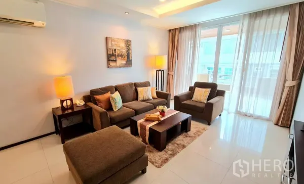 Apartment for rent in Watthana, Bangkok - Bright living room with brown sofa set, warm lamps, floor-to-ceiling windows and balcony access.