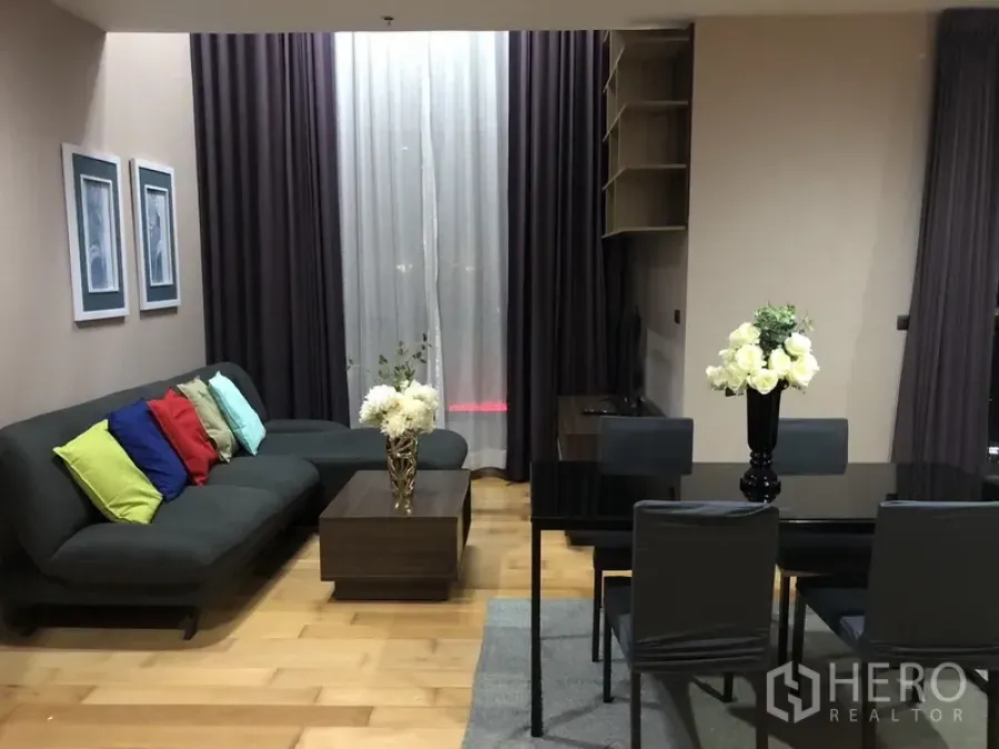 公寓 出租或出售在Khlong San, Bangkok - 客餐厅一体空间，L型沙发、黑色玻璃餐桌与落地窗帘。