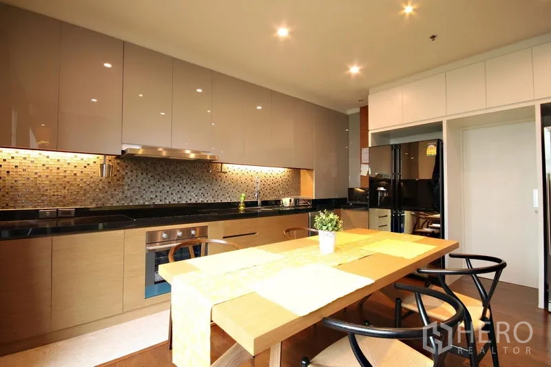 Condominium for rent or sale in Khlong Toei, Bangkok - Modern kitchen with glossy cabinets, a dining table, and under-cabinet lighting.