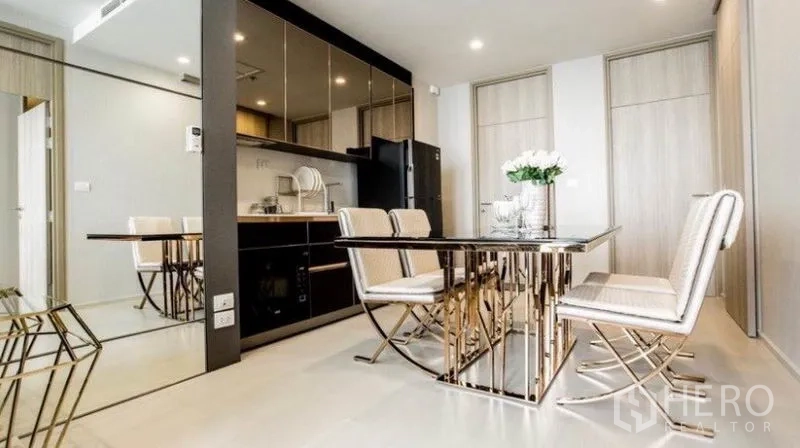 Condominium for rent in Pathum Wan, Bangkok - Dining area with mirrored wall, marble-top table and four upholstered chairs beside open kitchen.