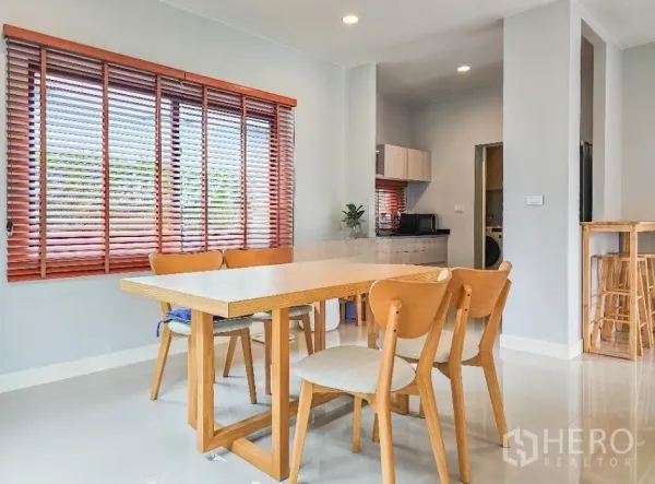 Detached House for sale in Lam Luk Ka, Pathum Thani - Dining area with wooden table and chairs next to window blinds and a pantry counter.