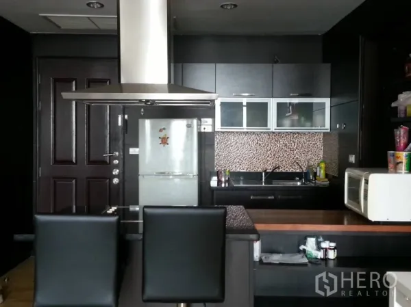 Condominium for rent in Khlong San, Bangkok - Kitchen view showing breakfast bar with stools, refrigerator, microwave and built‑in cabinetry.
