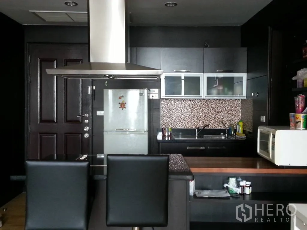 Condominium for rent in Khlong San, Bangkok - Kitchen view showing breakfast bar with stools, refrigerator, microwave and built‑in cabinetry.