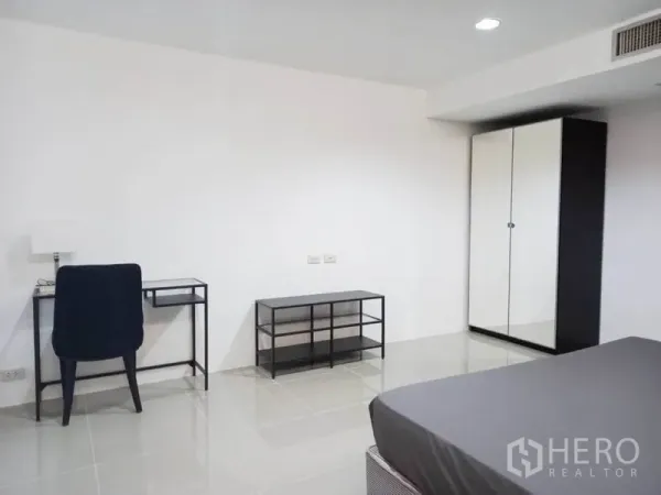 Condominium for rent in Khlong Toei, Bangkok - Spacious bedroom with a desk, black chair, media console and mirrored wardrobe.