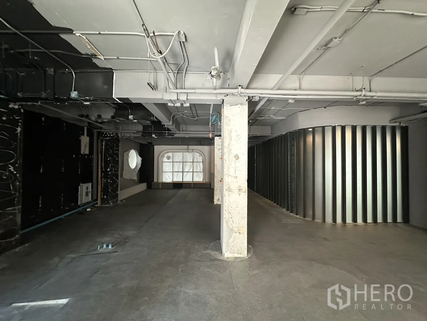 พื้นที่ขายของ for rent in Watthana, Bangkok - พื้นร้านว่างกว้าง มีเสากลาง ผนังโลหะโค้ง และหน้าต่างโชว์ทรงโค้ง.