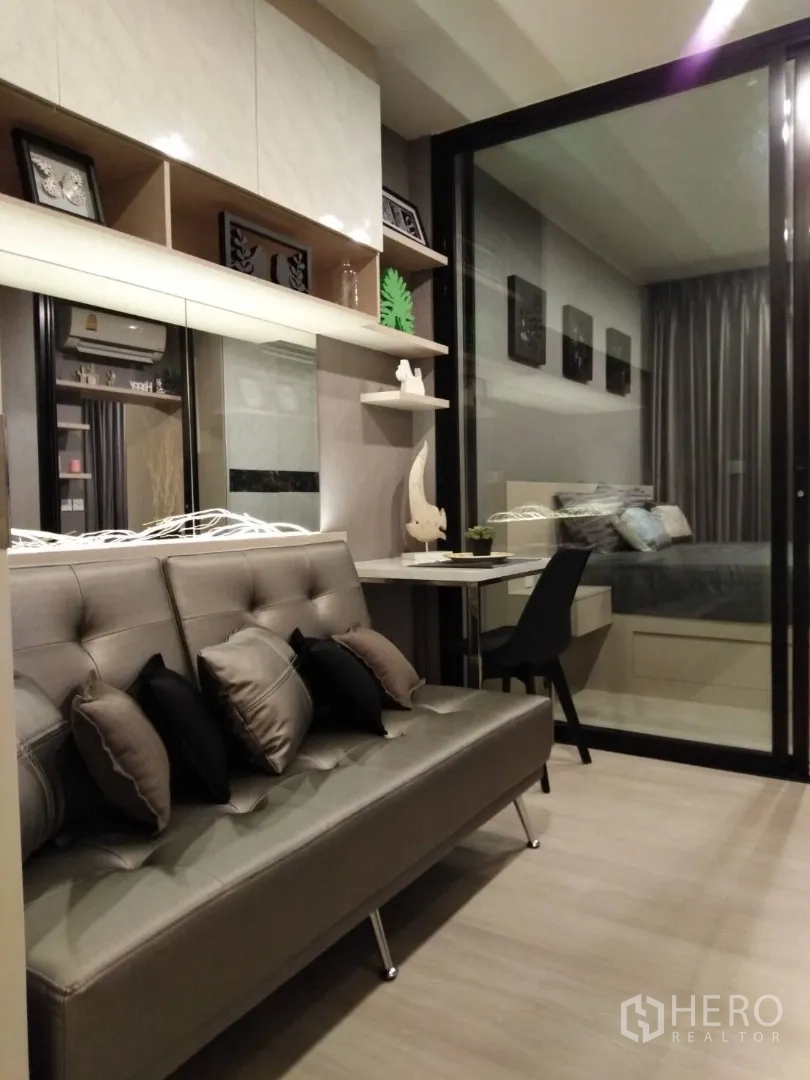 คอนโด ให้เช่าในHuai Khwang, Bangkok - มุมนั่งเล่นโซฟาหนังสีเทา ชั้นวางของ และโต๊ะทำงานหันเข้าหาห้องนอน