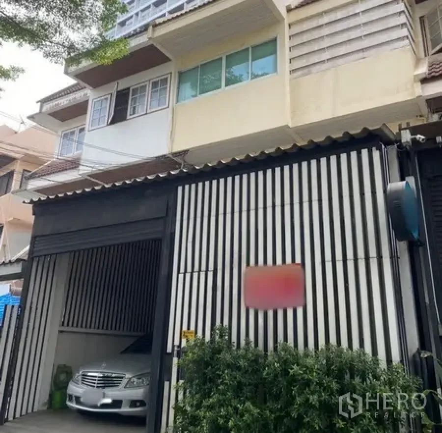 ทาวน์เฮาส์ ให้เช่าในWatthana, Bangkok - ภายนอกทาวน์เฮ้าส์เขตวัฒนา กรุงเทพฯ ประตูแนวตั้ง ที่จอดรถในร่ม และไม้พุ่มด้านหน้า