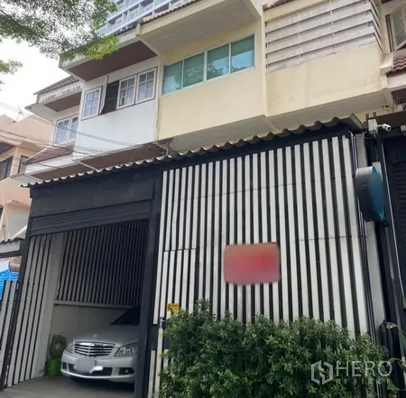 ทาวน์เฮาส์ ให้เช่าในWatthana, Bangkok - ภายนอกทาวน์เฮ้าส์เขตวัฒนา กรุงเทพฯ ประตูแนวตั้ง ที่จอดรถในร่ม และไม้พุ่มด้านหน้า