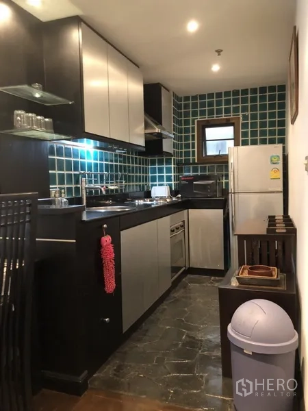 公寓 出租在Watthana, Bangkok - 公寓厨房，绿色瓷砖墙面，黑色橱柜，带灶台、抽油烟机和冰箱。
