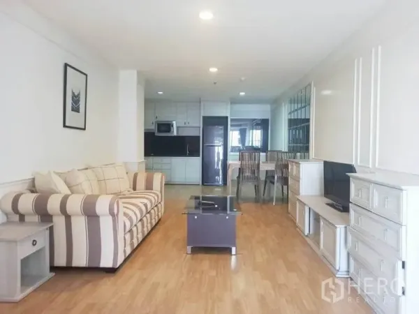 Condominium for rent in Khlong Toei, Bangkok - Bright open-plan living room with striped sofa, TV console, and a fitted kitchen in a Bangkok condo.