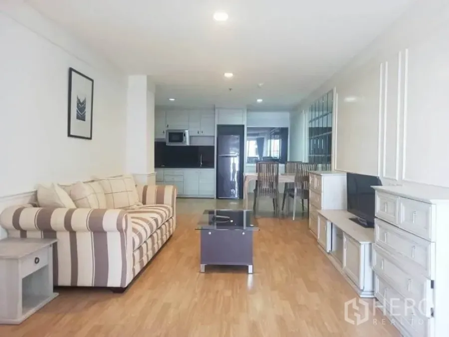 Condominium for rent in Khlong Toei, Bangkok - Bright open-plan living room with striped sofa, TV console, and a fitted kitchen in a Bangkok condo.