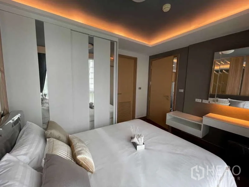 Condominium for sale in Watthana, Bangkok - Primary bedroom with cove lighting, sliding wardrobe doors and vanity in neutral tones.
