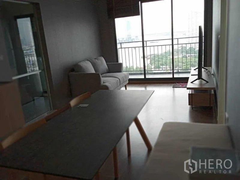 公寓 出租在Yan Nawa, Bangkok - 开放式客厅，配沙发、餐桌和电视，通向可观河景的阳台。
