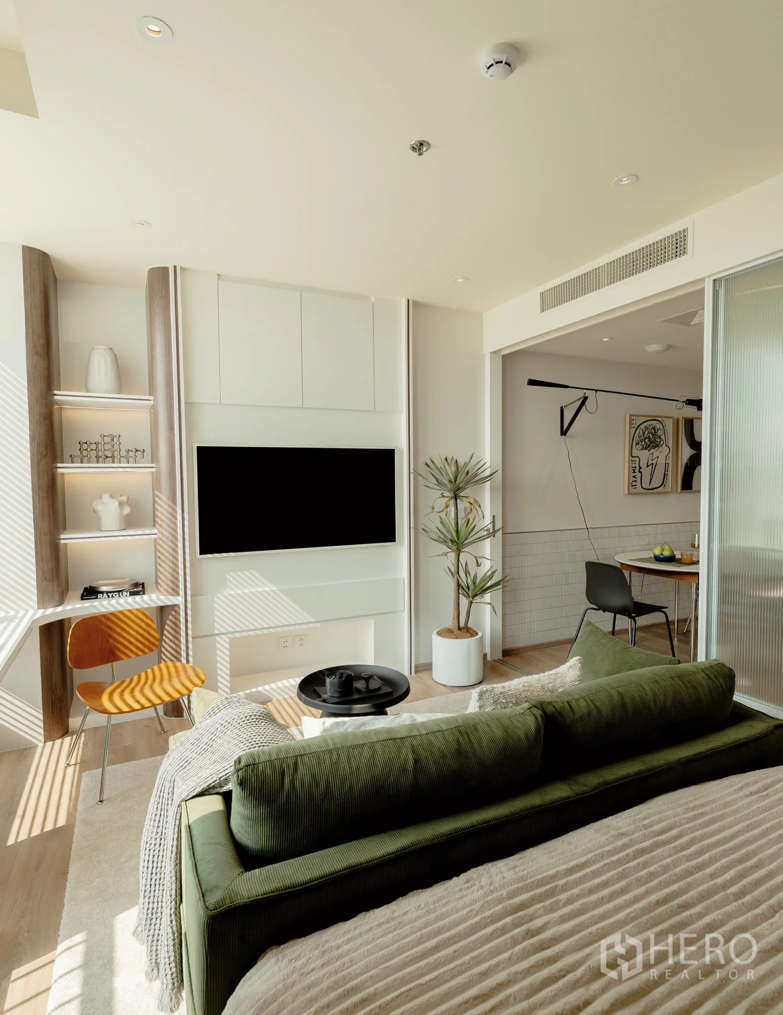 คอนโด for rent in Watthana, Bangkok - พื้นที่นั่งเล่นและพื้นที่นอนสว่างด้วยแสงธรรมชาติ โซฟาสีเขียว เตียง ทีวีบิลต์อิน โต๊ะทำงาน กระถางต้นไม้ และประตูกระจกสไลด์เชื่อมครัว