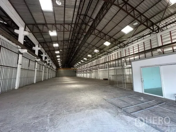 Warehouse for rent in Lam Luk Ka, Pathum Thani - Long, column-free storage area with metal wall panels, high ceiling, skylights, and an attached office module.
