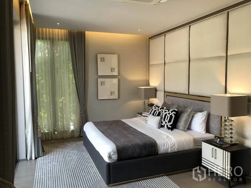 บ้าน ขายในBang Kapi, Bangkok - ห้องนอนหลักผนังหัวเตียงบุพิเศษ หน้าต่างสูง ผ้าม่านโปร่ง และไฟสลัวอบอุ่น.