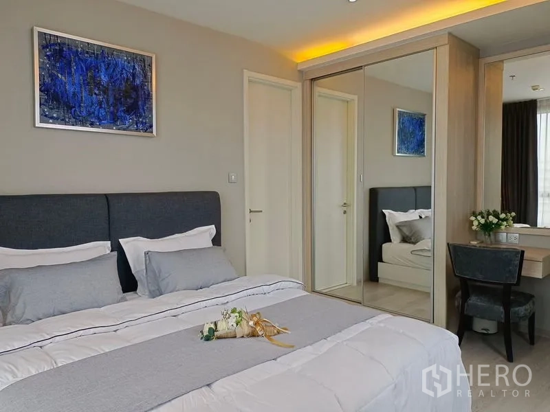 Condominium for rent in Watthana, Bangkok - Bedroom detail with grey headboard, artwork and built-in mirrored wardrobe with dressing table.