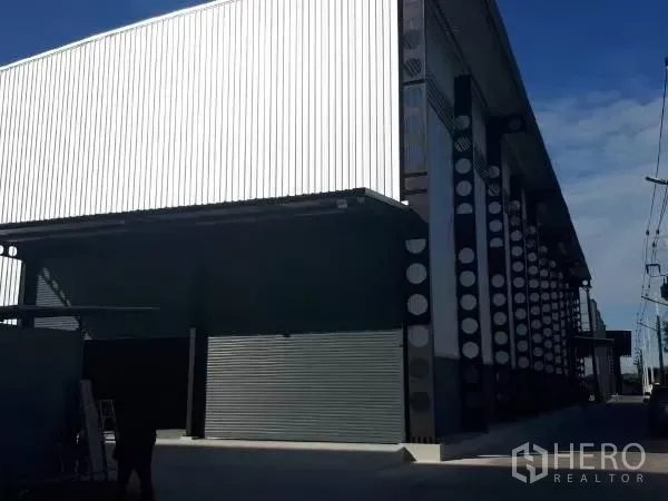 Warehouse for rent in Khlong Sam Wa, Bangkok - Modern warehouse exterior with corrugated metal cladding, steel columns, and a roller shutter loading bay.