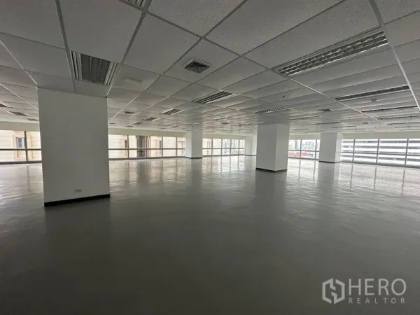 办公空间 出租 - 宽敞空置办公内景，立柱、吊顶、荧光灯与环幕窗。