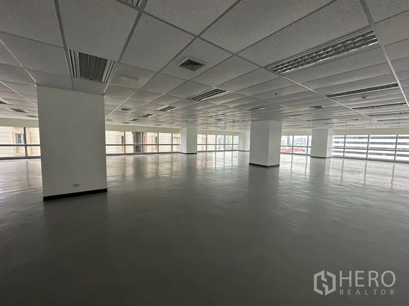 办公空间 出租 - 宽敞空置办公内景，立柱、吊顶、荧光灯与环幕窗。