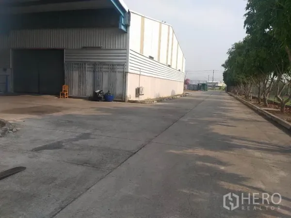 货栈 出租在Pathum Thani - 仓库侧面装卸区与卷闸门，旁有绿树车道