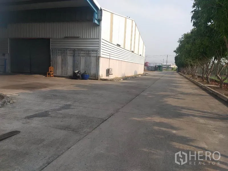 货栈 出租在Pathum Thani - 仓库侧面装卸区与卷闸门，旁有绿树车道