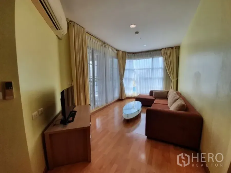 Condominium for rent in Khlong Toei, Bangkok - Bright corner living room with floor-to-ceiling windows, L-shaped sofa, TV console and wood flooring.