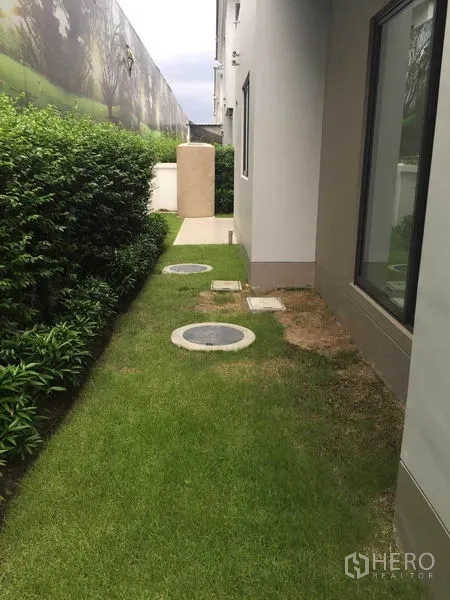 独立式住宅 出售在Pak Kret, Nonthaburi - 房侧花园，整齐绿篱、草坪与检查井盖