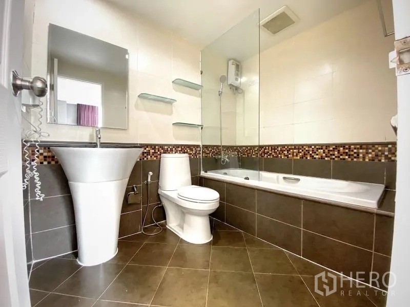 Condominium for rent in Khlong Toei, Bangkok - Modern bathroom with pedestal sink, toilet, bathtub with glass screen and mosaic trim.