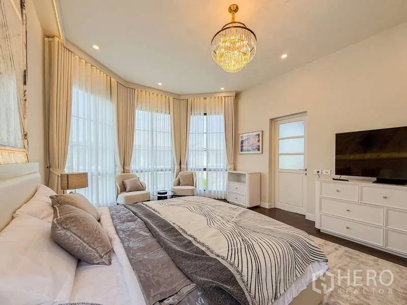 Detached House for rent or sale in Bang Kapi, Bangkok - Master bedroom view with chandelier, TV cabinet and lounge chairs beside tall windows.