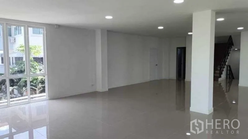带办公室的家 出售在Huai Khwang, Bangkok - 宽敞的一层工作区，大窗、白色柱子和通往楼上的楼梯。