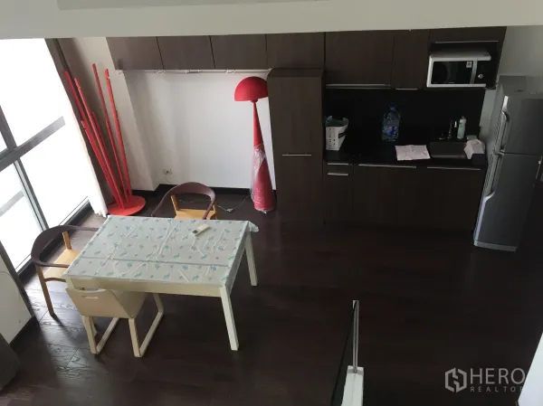 公寓 出租在Ratchathewi, Bangkok - 紧凑厨房，深色橱柜、微波炉与冰箱，旁有临窗餐桌。