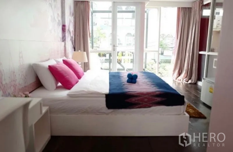 Townhouse for rent in Khlong Toei, Bangkok - Double bedroom with pink cushions and balcony windows bringing natural light.