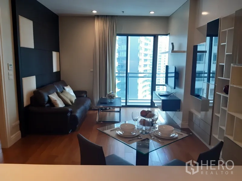 Condominium for rent in Khlong Toei, Bangkok - Khlong Toei condo living room with leather sofa, wall-mounted TV and balcony city view through sliding glass doors.