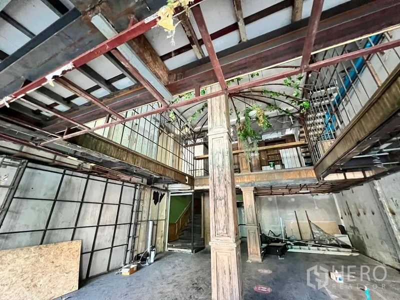 Shophouse for rent in Watthana, Bangkok - Wide unfinished hall showing exposed steel beams, mezzanine structure, and large wooden doors.