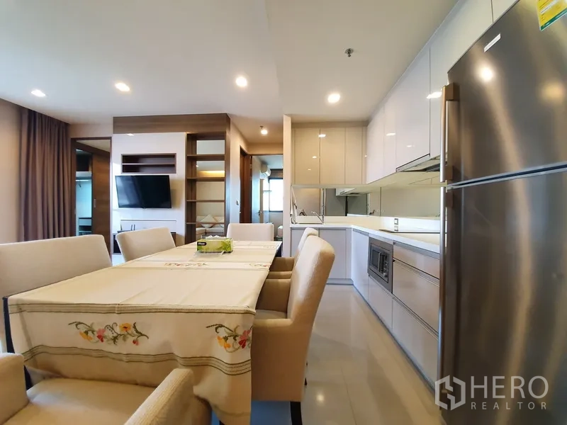 Condominium for rent in Bang Rak, Bangkok - Bright kitchen with built-in cabinets, stainless-steel fridge, and dining area under recessed lighting.