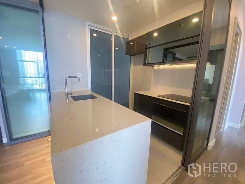 Condominium for rent in Bang Rak, Bangkok - Modern kitchen featuring a long quartz island with sink and induction cooktop.