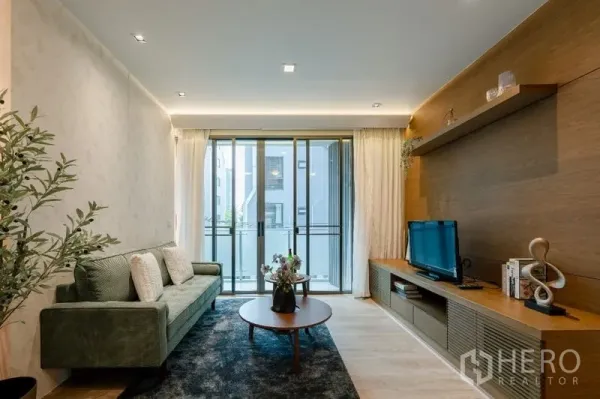 Condominium for sale - Bright living room with balcony doors, wood feature wall, TV console and green sofa.